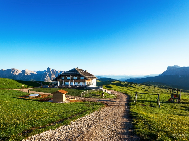 Die Pralongia-Hütte liegt weit oben auf einer grünen Wiese inmitten der Dolomitengipfel
